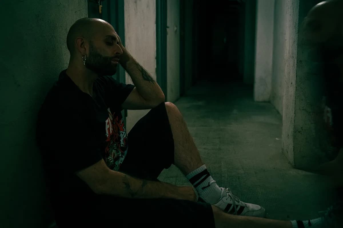 D-DOC seduto a terra contro il muro di un corridoio, la testa appoggiata alla mano